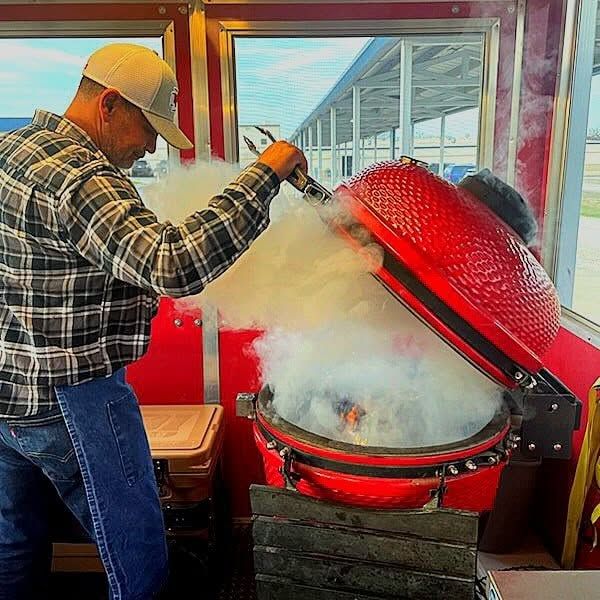Lifting the lid on a red smoker inside the Red Cooler BBQ trailer as smoke rolls out.